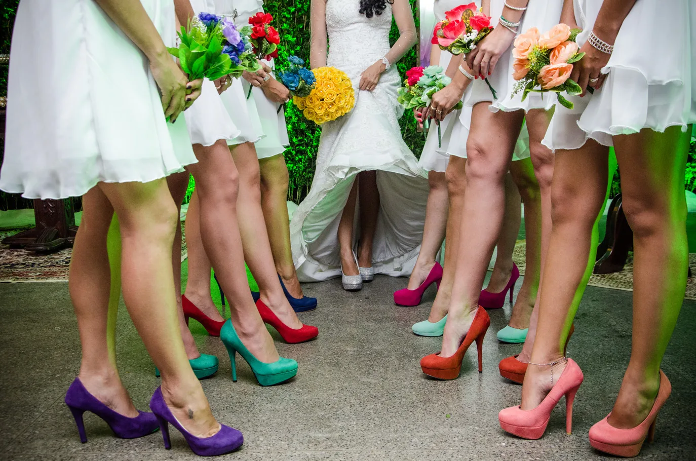 Madrinhas de vestidos claros com buquês e sapatos coloridos