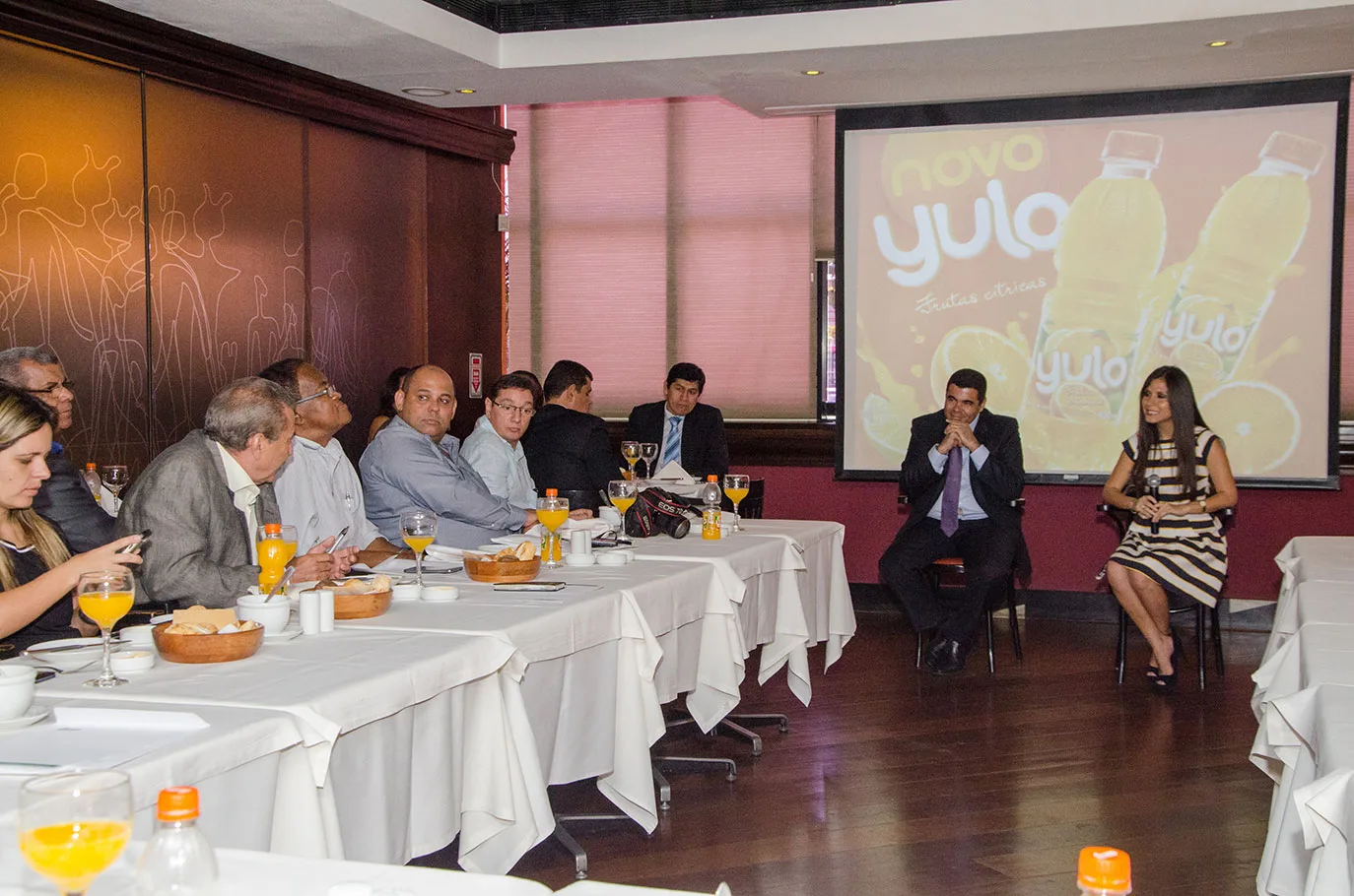 Apresentação institucional para convidados sentados à mesa em encontro empresarial
